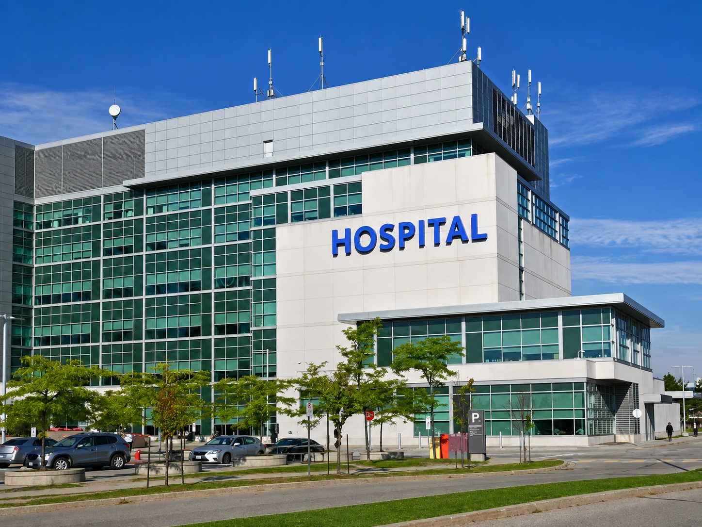 Modern hospital building with green glass facade and blue signage under a clear sky
